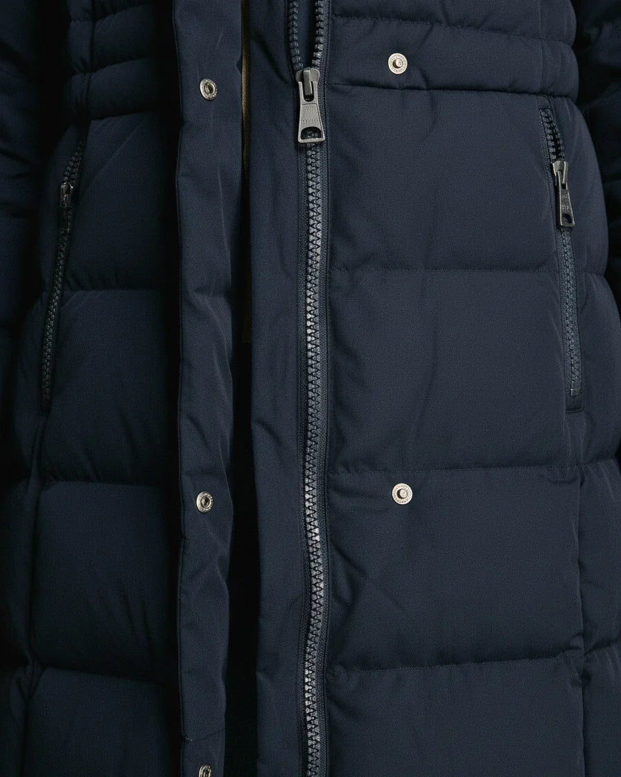 Long navy blue quilted puffer coat with a plush-trimmed hood and zippered pockets. - 7