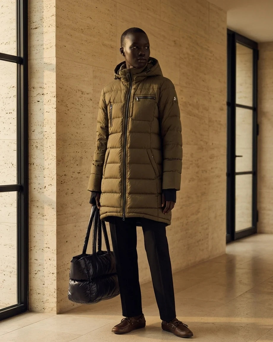 Mid-length olive green quilted puffer coat with a hood and black zipper details on a model.