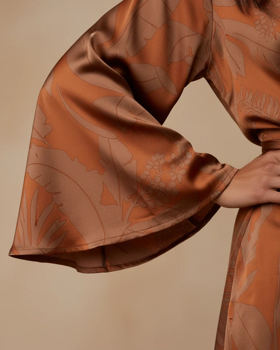 Model wearing a rust-colored mini wrap dress with a leaf print, featuring wide kimono sleeves and a waist tie. - 4