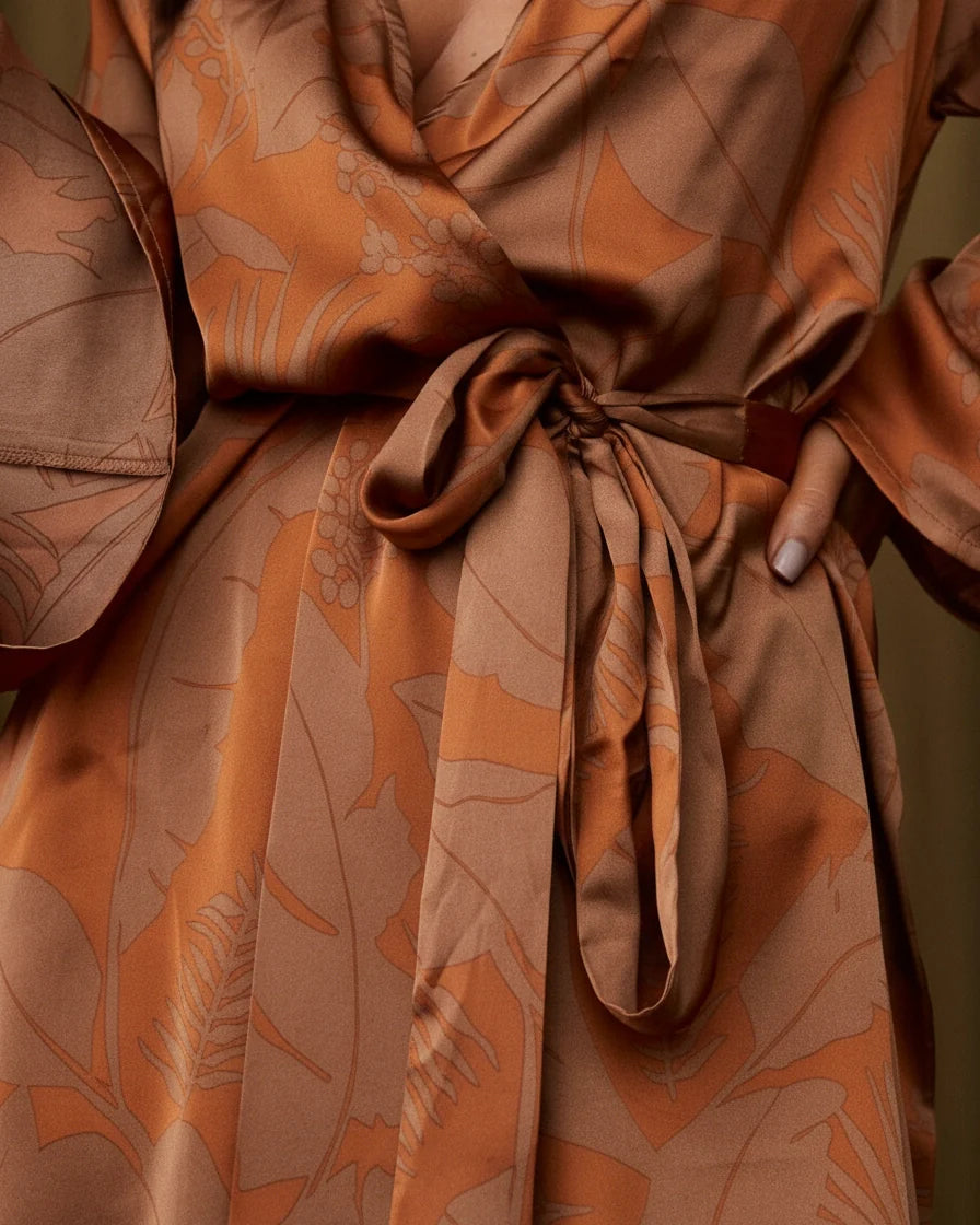 Model wearing a rust-colored mini wrap dress with a leaf print, featuring wide kimono sleeves and a waist tie. - 5