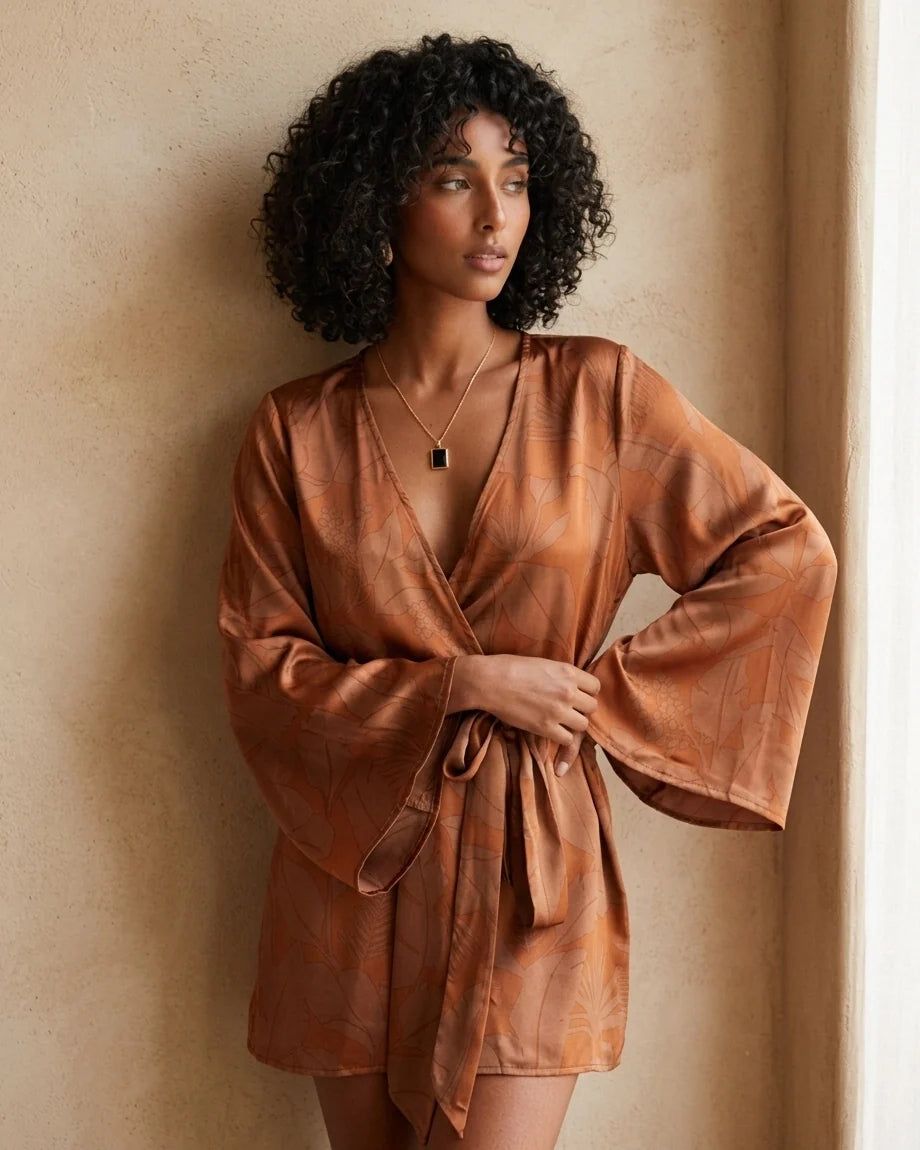 Model wearing a rust-colored mini wrap dress with a leaf print, featuring wide kimono sleeves and a waist tie.