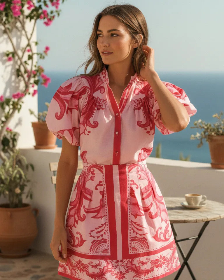Woman wearing a printed two-piece set with a buttoned puff-sleeve top and a short pleated skirt - Red