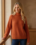 Model wearing a relaxed orange knit sweater with a mock neck and drop shoulders.