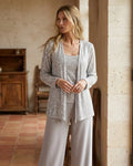 A three-piece silver evening set featuring a sequined lace open jacket, matching square-neck top, and flowing wide-leg trousers.